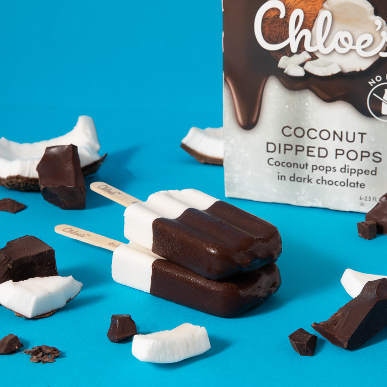 coconut dipped pops on a blue background with the coconut dipped box in the background and coconut and chocolate pieces around