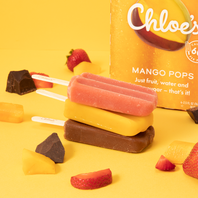 strawberry, mango, chocolate pops stacked on a yellow background with a mango box in the background and fruit and chocolate pieces
