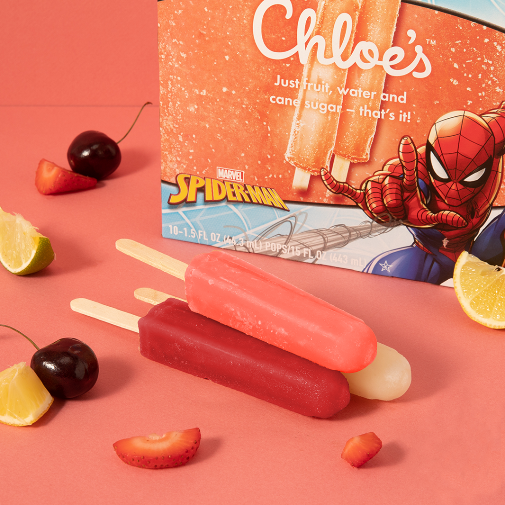 kids pops stacked on a pink background with spider-man box in the background and pieces of lemon, cherry, and strawberries around